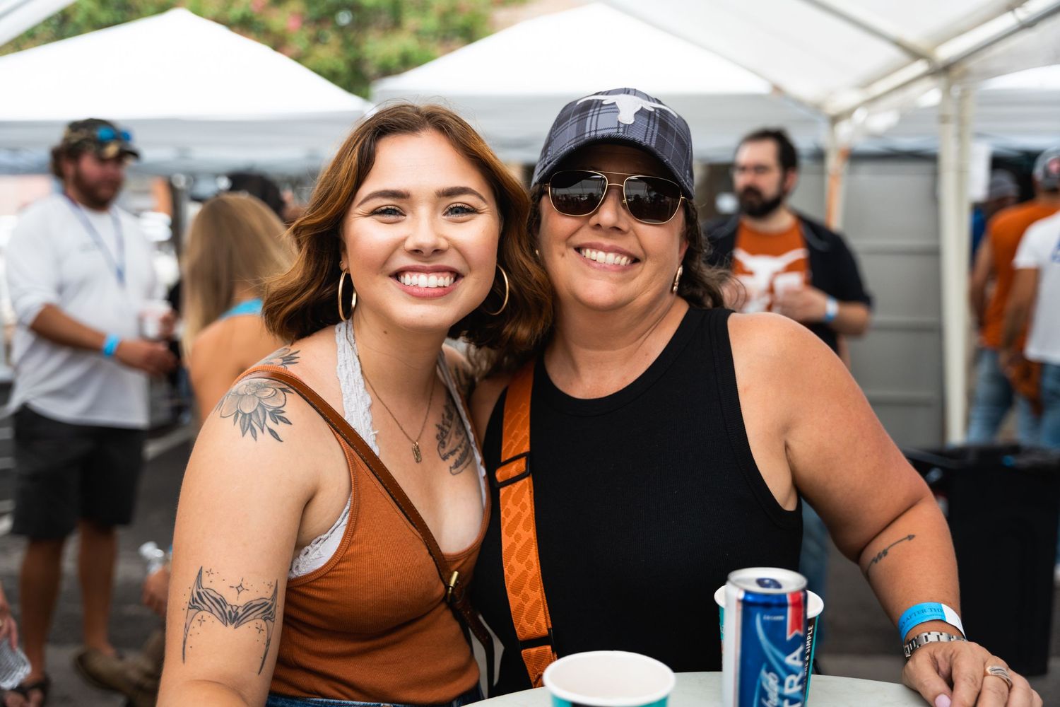 Two festival attendees posing together with drinks at an outdoor event.