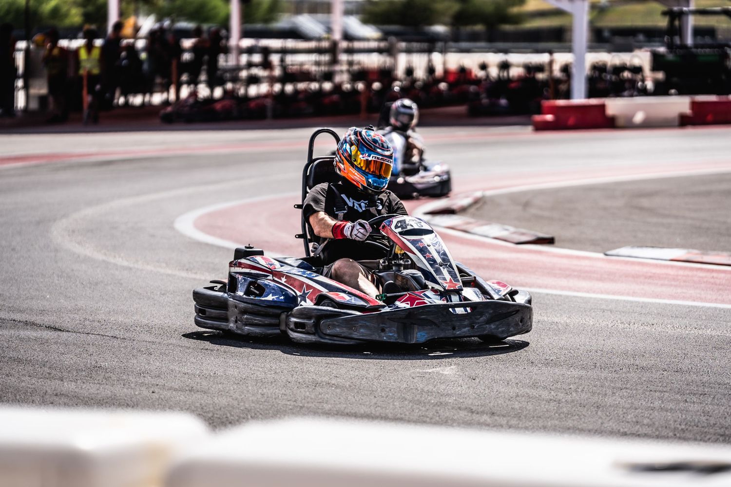 Racing go-kart taking sharp turn on professional karting circuit with red barriers.