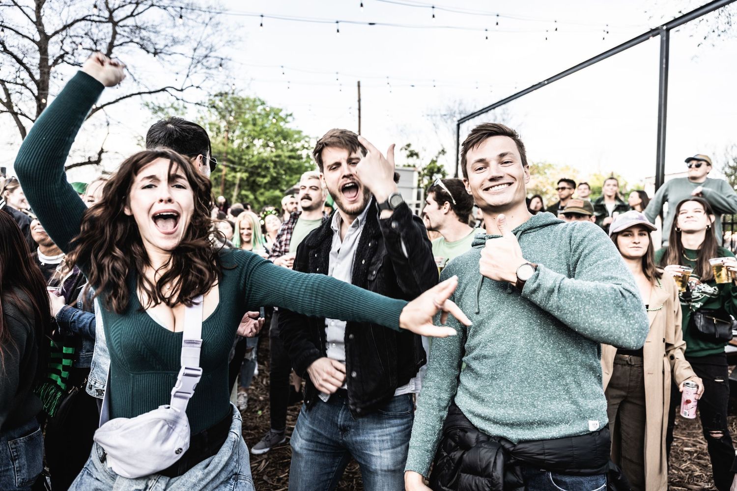 Energetic crowd celebrates at outdoor music festival with string lights visible overhead.