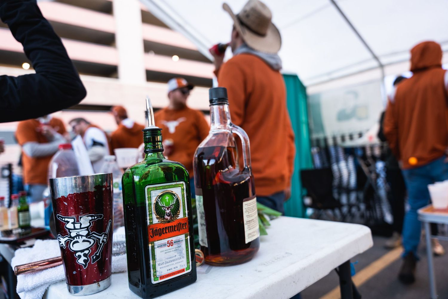 Liquor bottles displayed on a table at an outdoor event with people mingling in the background.