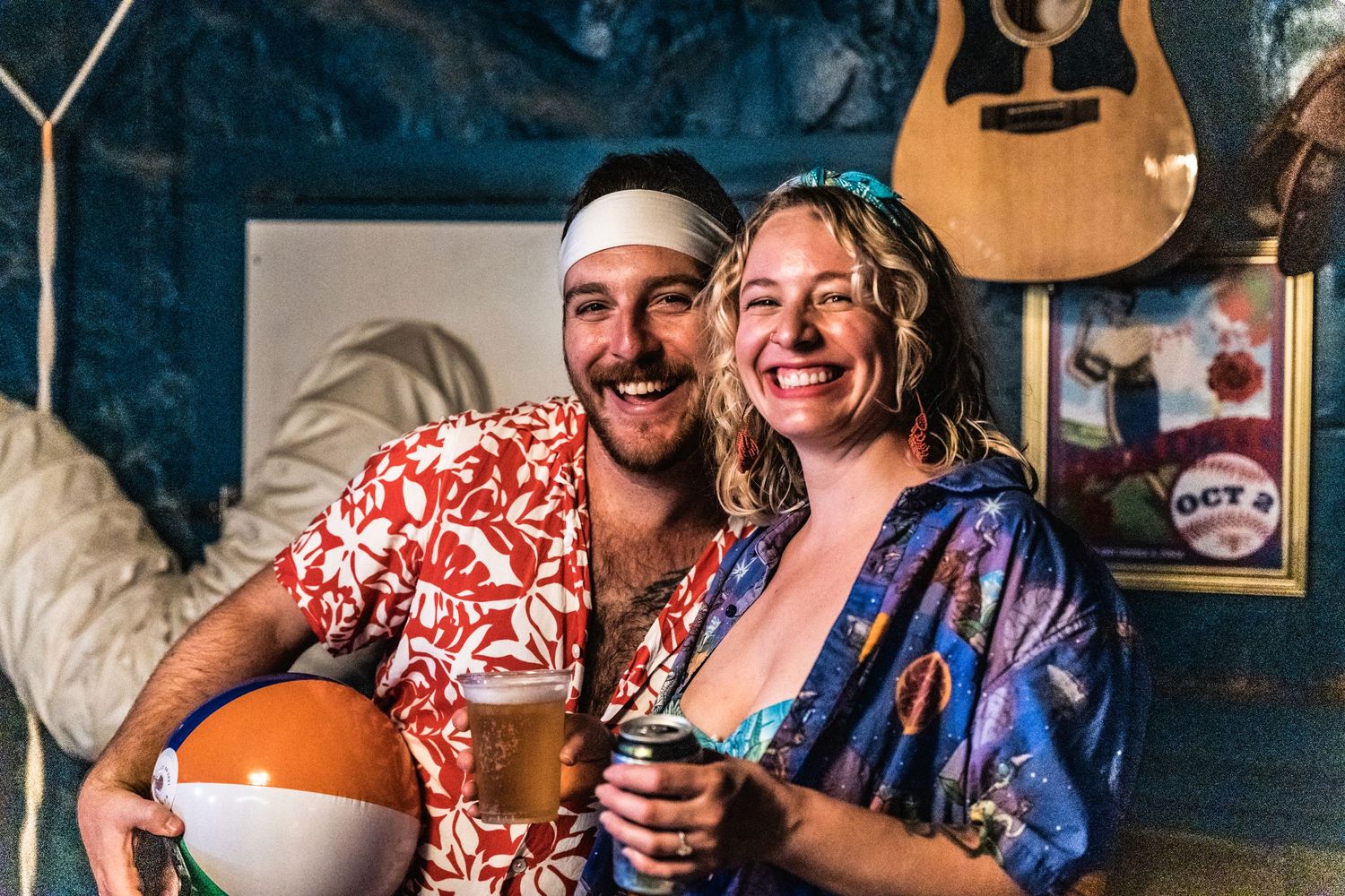 A couple in casual Hawaiian shirts enjoying drinks together at a bar with a guitar hanging on the wall behind them.