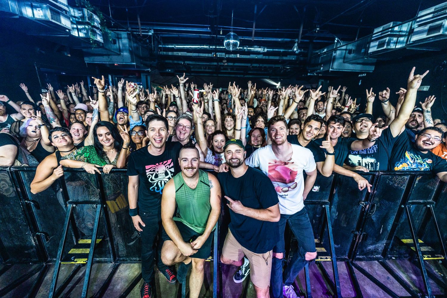 Large group of concert attendees pose together for group photo at music venue.