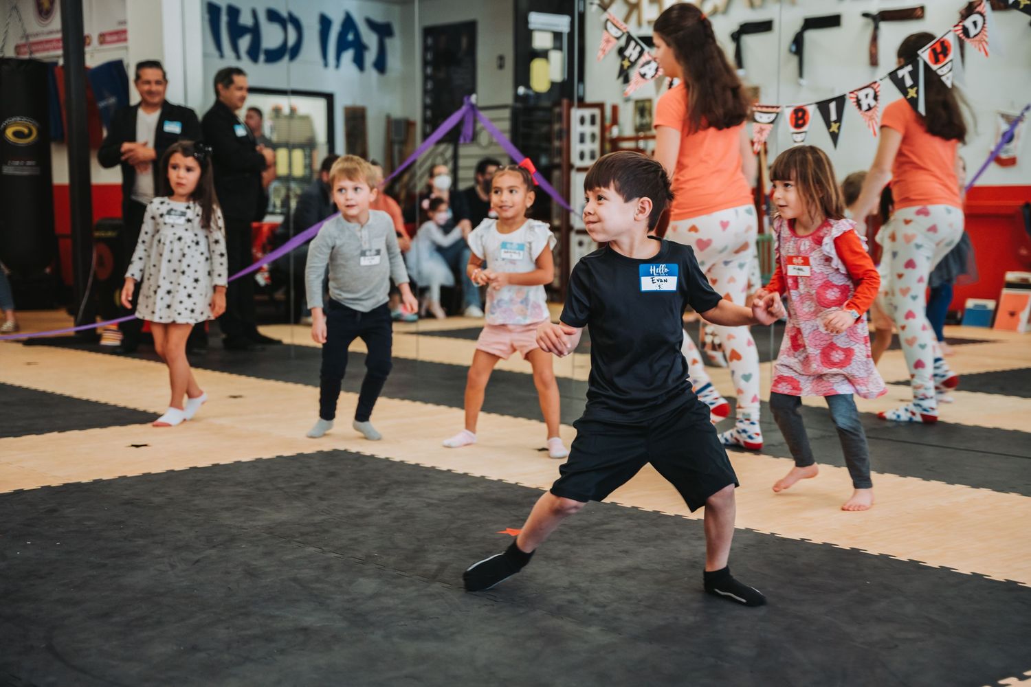 Young students practicing martial arts stances and movements on padded floor mats.