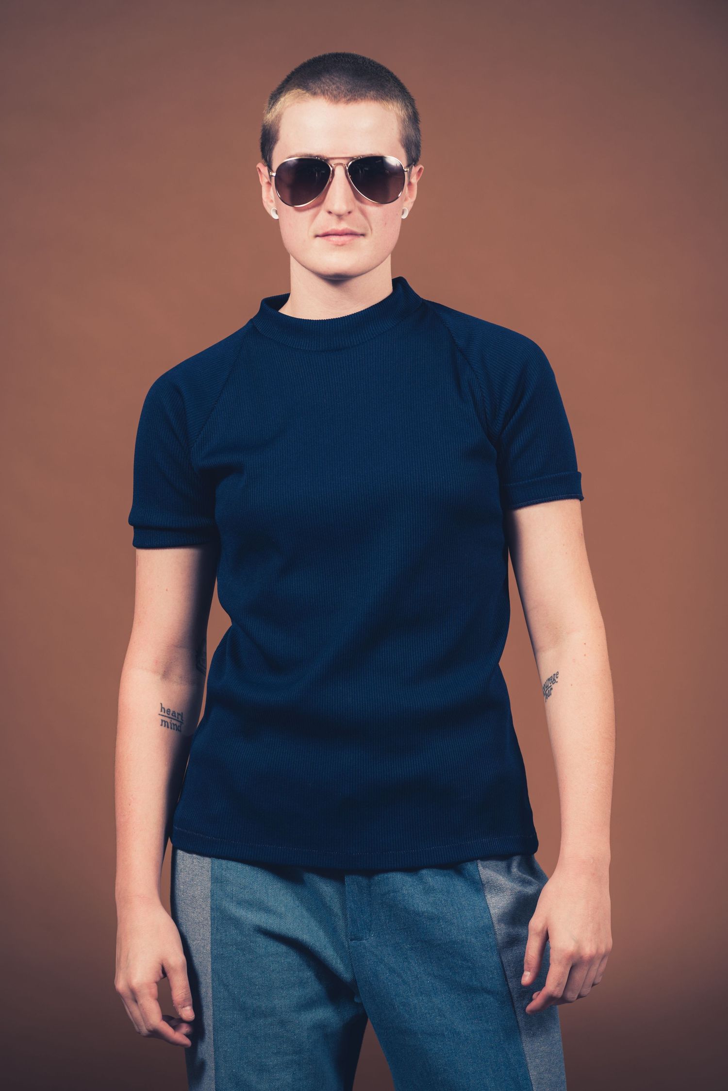 Portrait of person in fitted navy t-shirt and patchwork denim wearing aviator sunglasses.