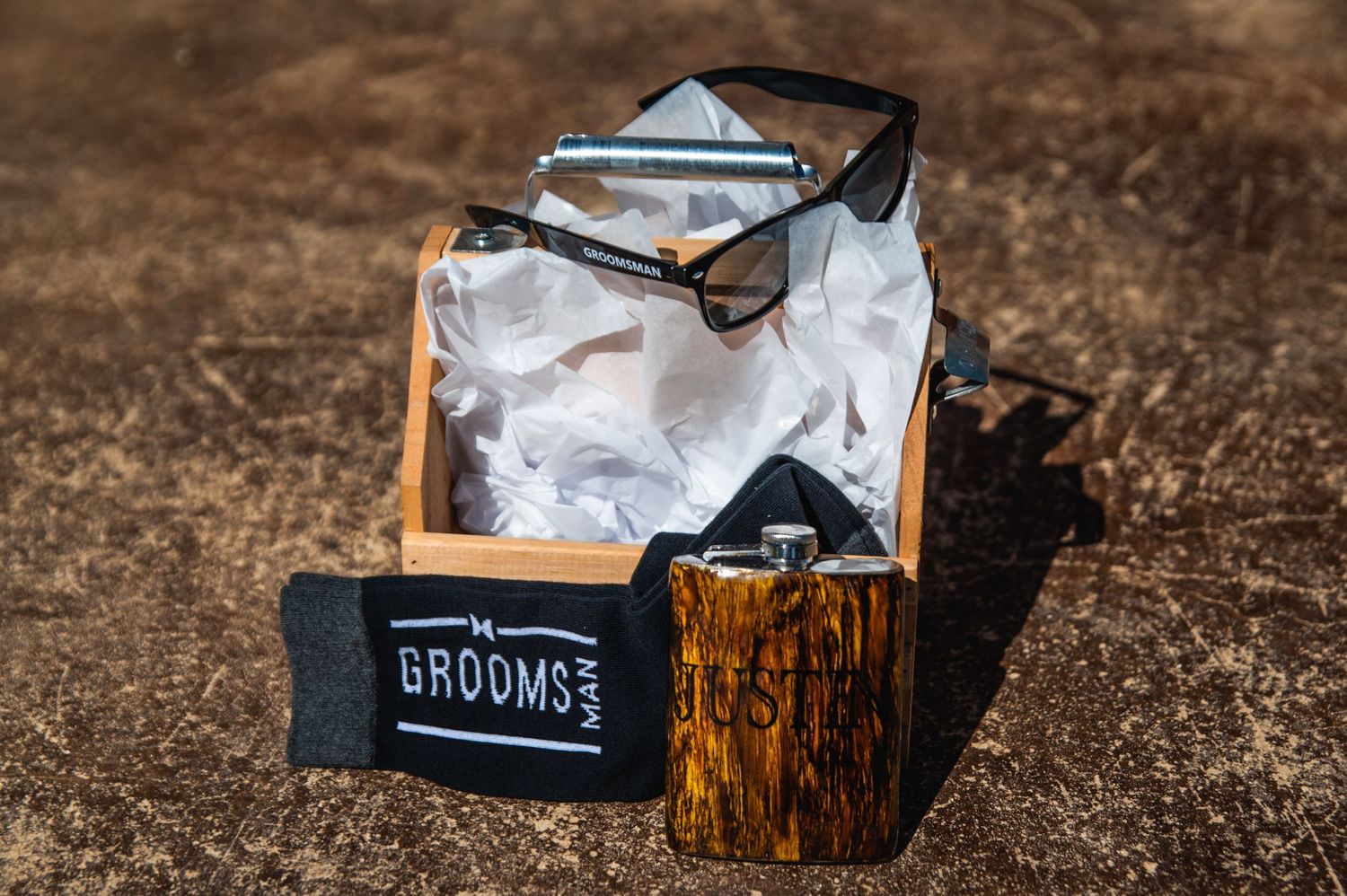 Groomsman gift box with sunglasses and wooden accents on rustic surface.
