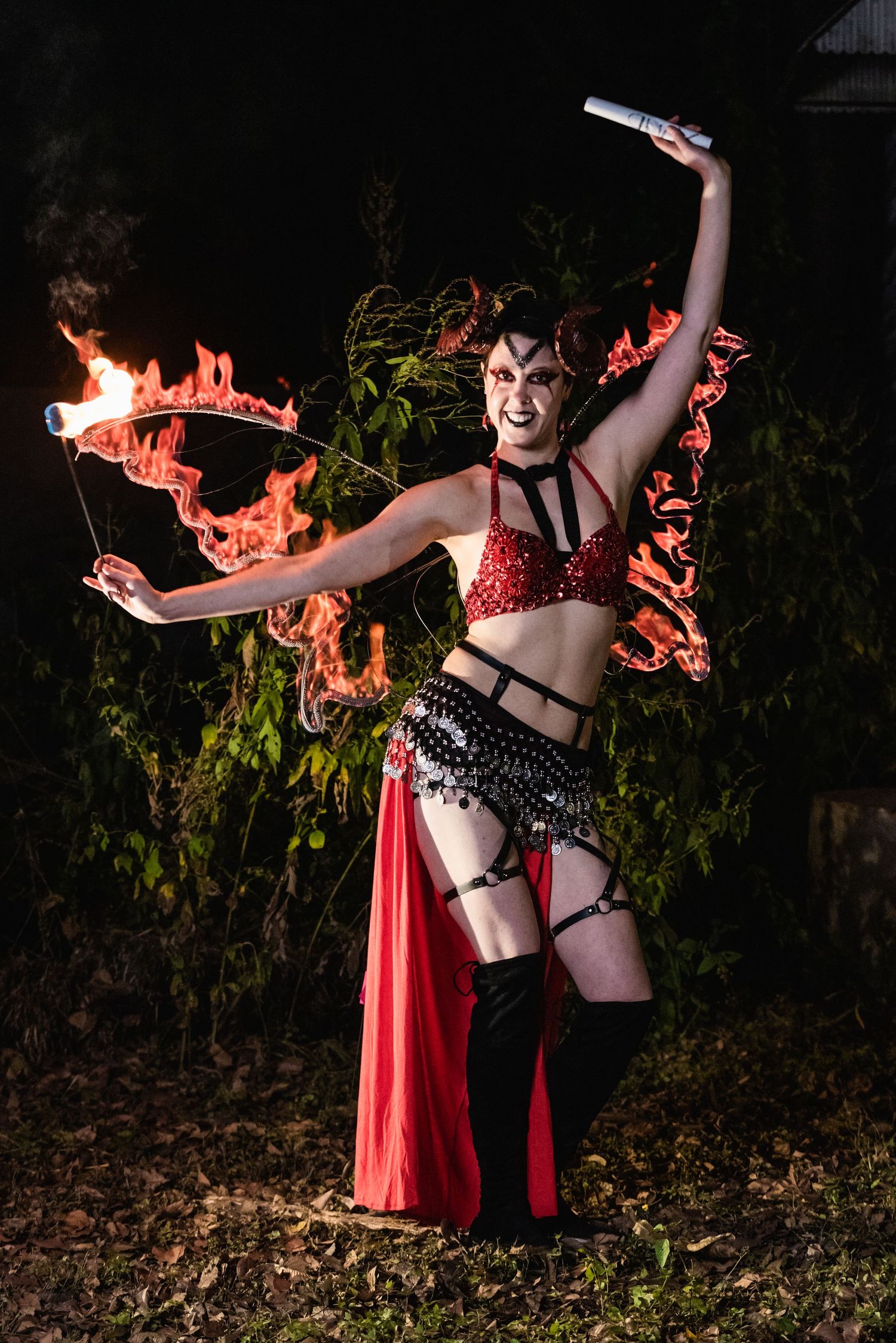 Fire dancer performs with dual flame props wearing red and black burlesque costume.
