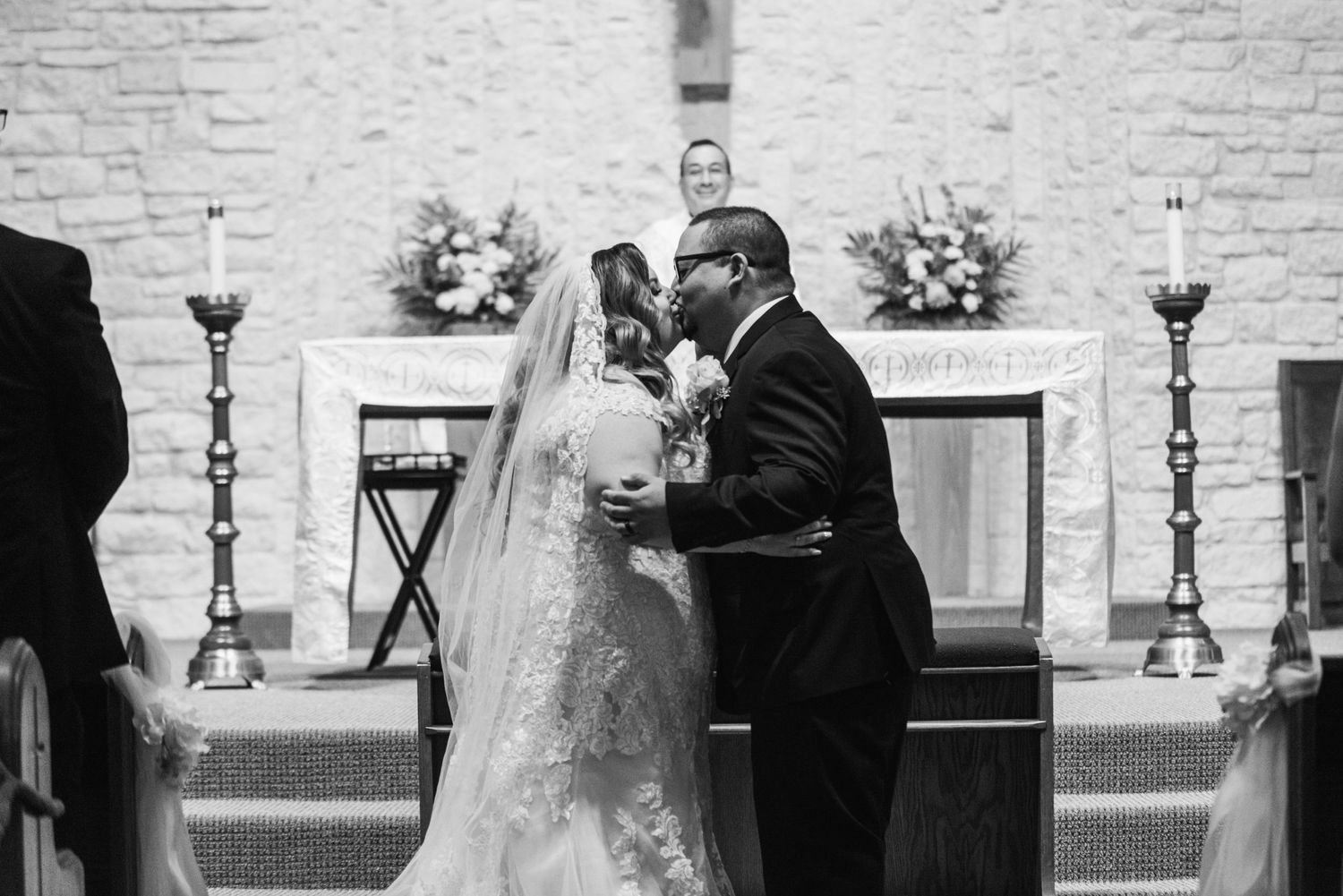 A couple shares an intimate moment during their wedding ceremony in a church with white brick walls.