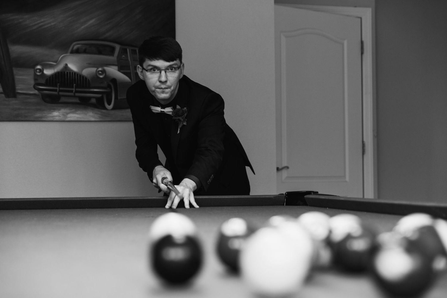 Black and white photo of someone playing pool, leaning over the table for a shot.