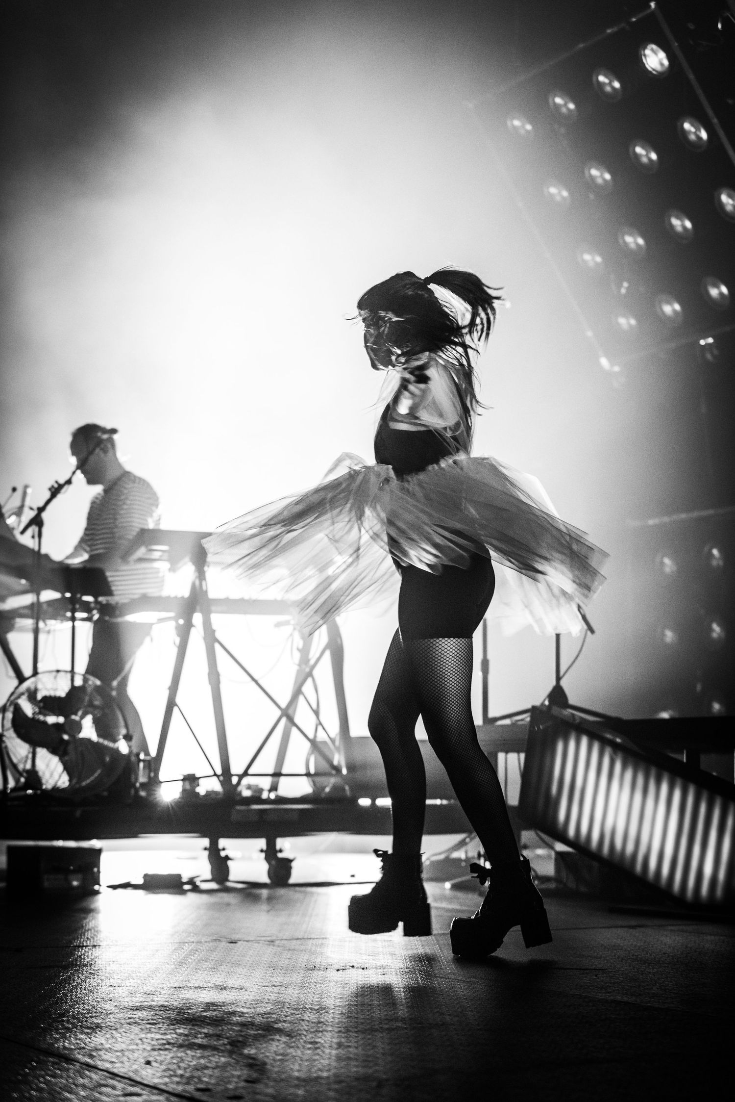 Silhouetted dancer in tulle skirt performs on stage with keyboard player in background.