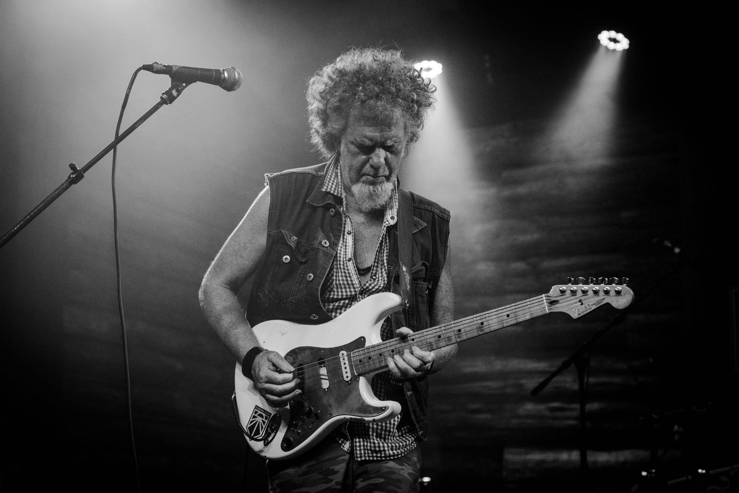 Dramatic black and white shot of guitarist playing electric guitar under stage spotlights.