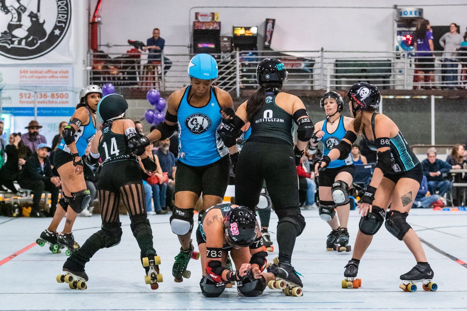 Roller derby players compete in a packed arena with spectators watching from the stands.