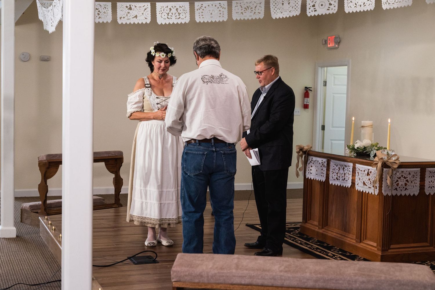 Wedding ceremony taking place in a simple room decorated with white papel picado-style banners.