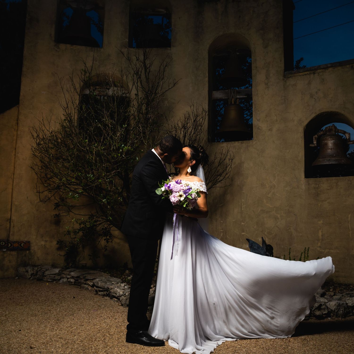 Dramatic wedding photo with the bride's dress billowing in front of a rustic church facade.