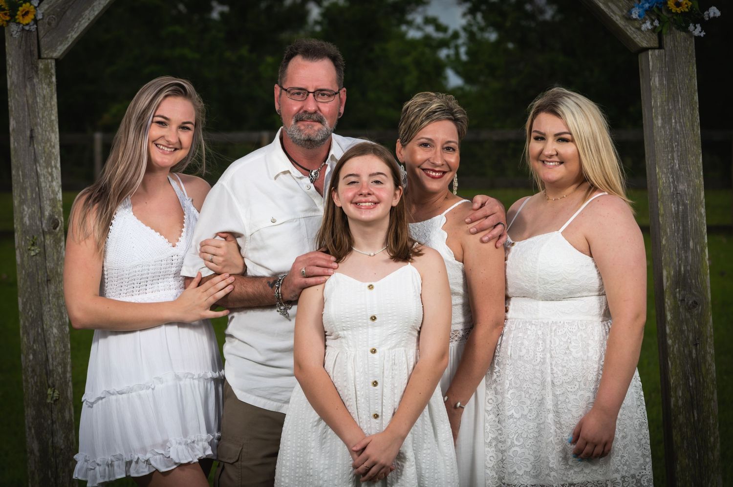 A group wearing coordinated white outfits poses together under a wooden archway.
