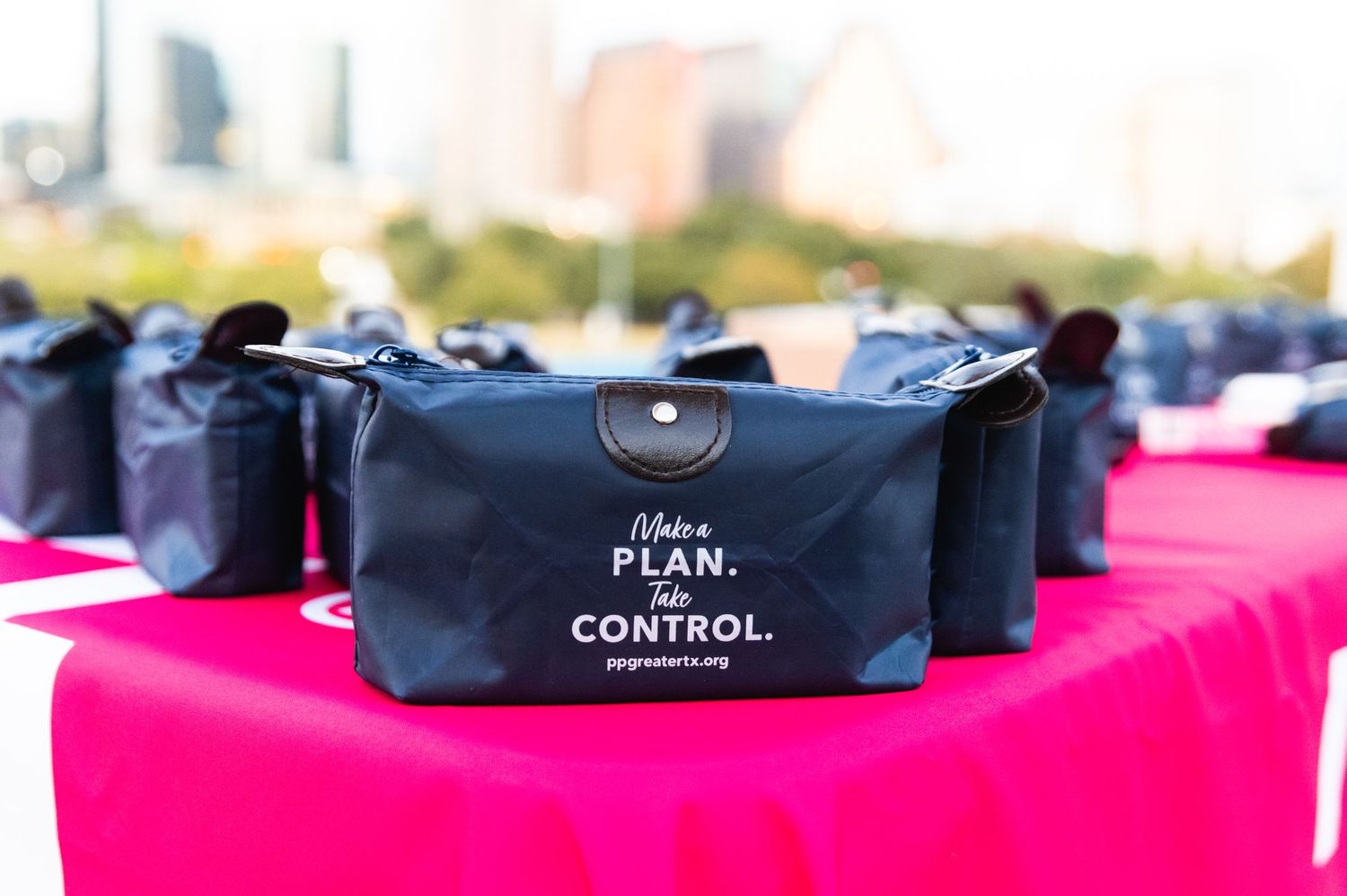 Black cosmetic bags arranged on pink tablecloth at event display.