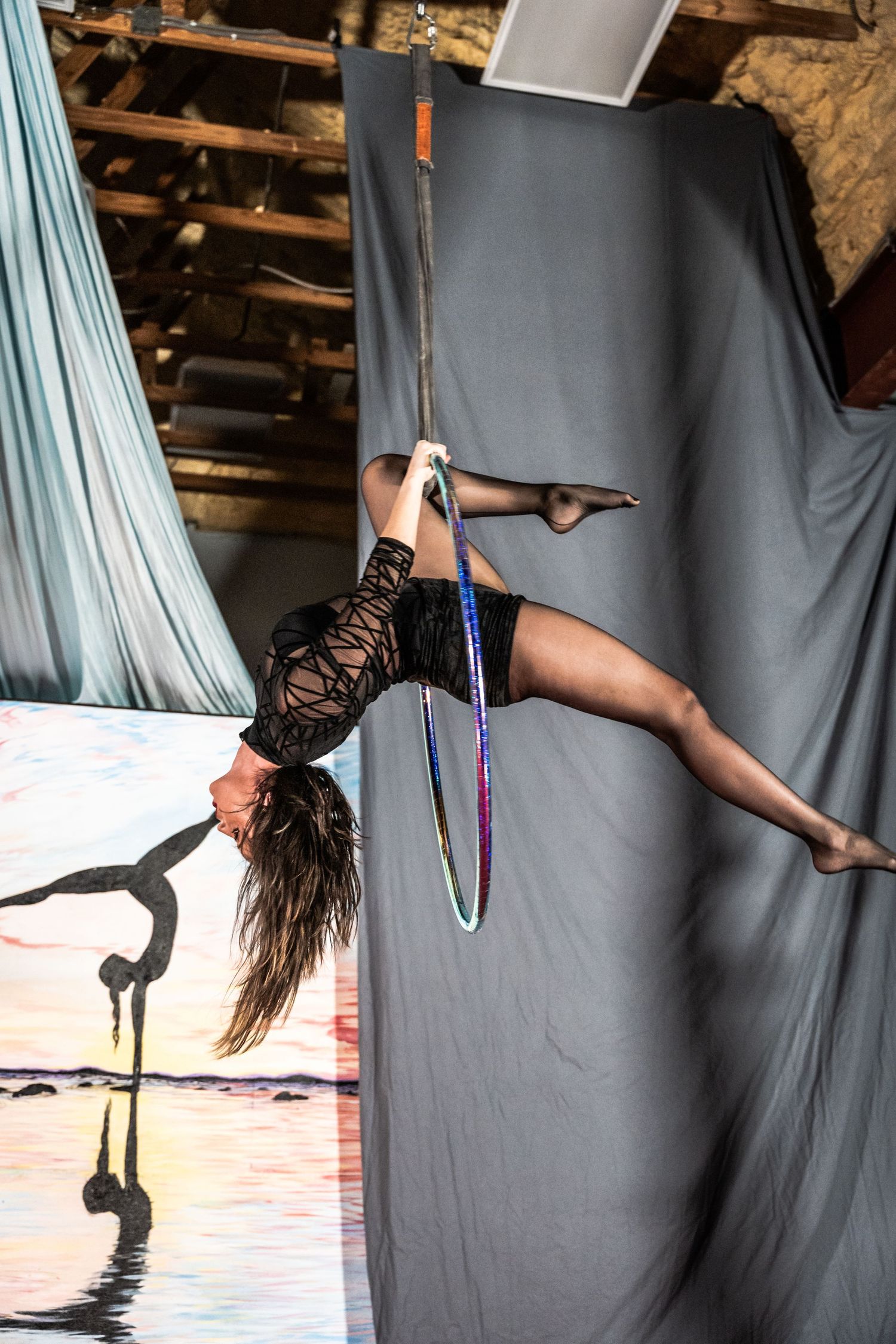 Aerial dancer performs with silk fabric against a dark background in dramatic lighting.