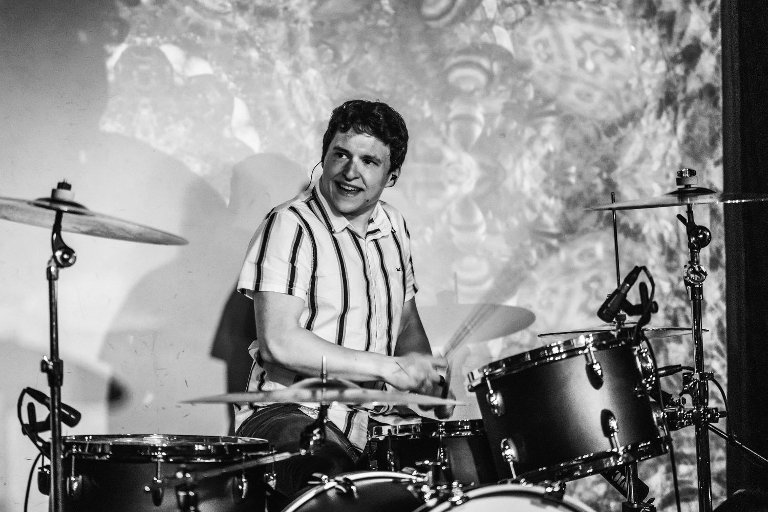 Black and white photo of a drummer performing on stage with dramatic lighting effects.
