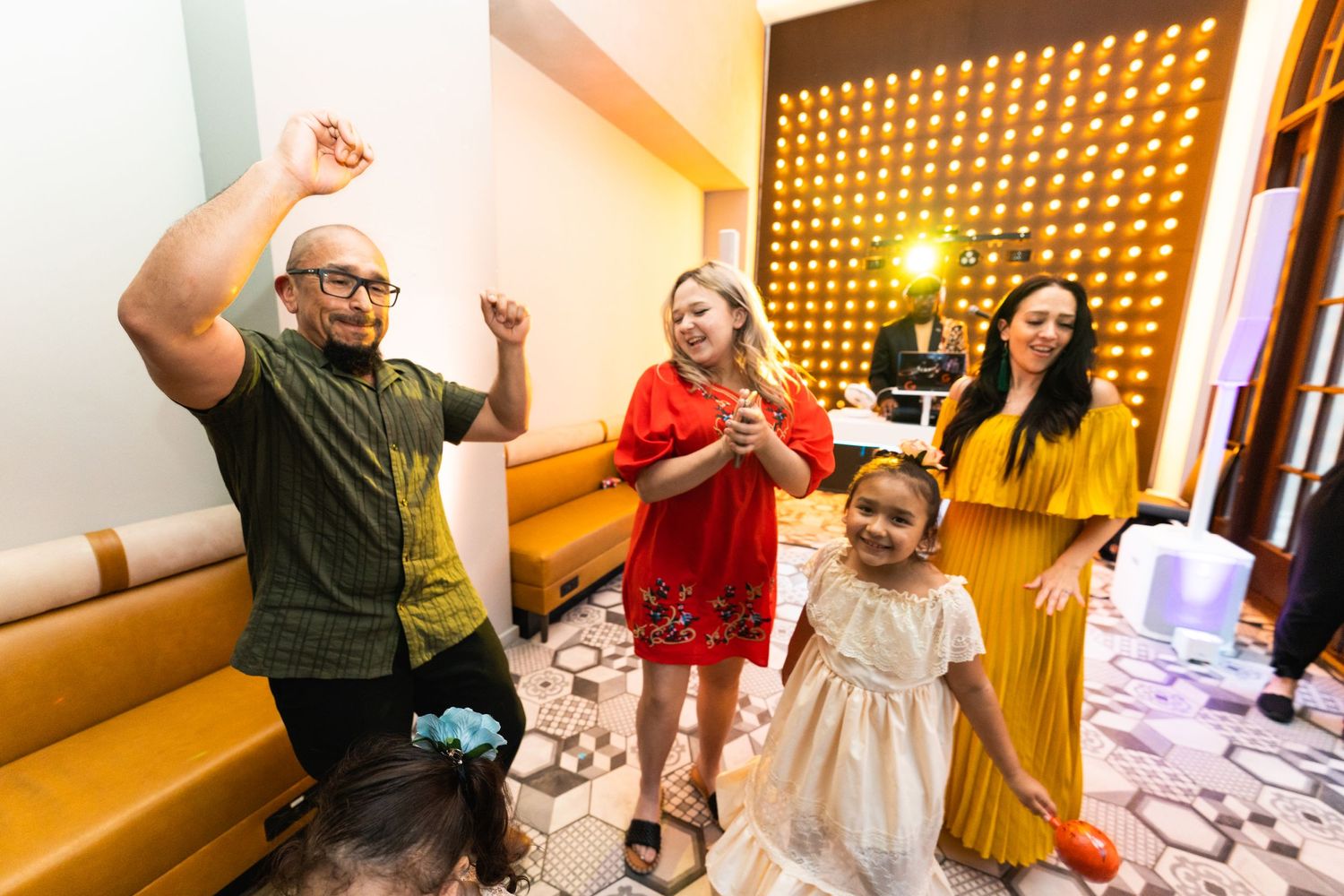 People dancing and celebrating with joyful expressions in a venue with decorative wall panels.