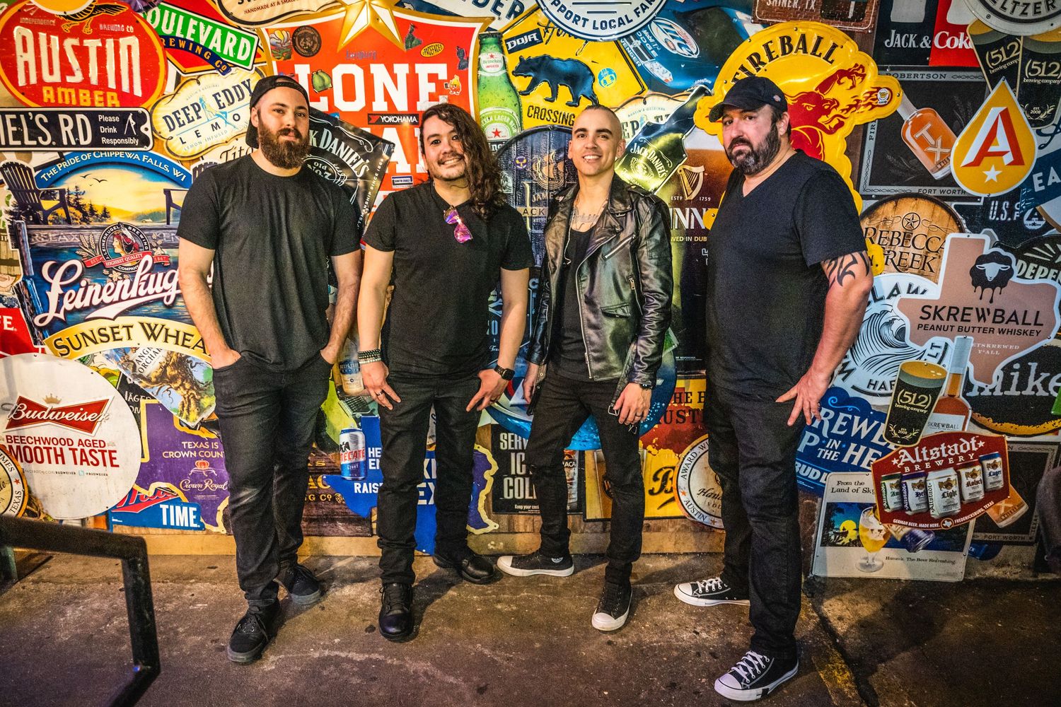 Rock band poses against wall covered in colorful music venue stickers and logos.
