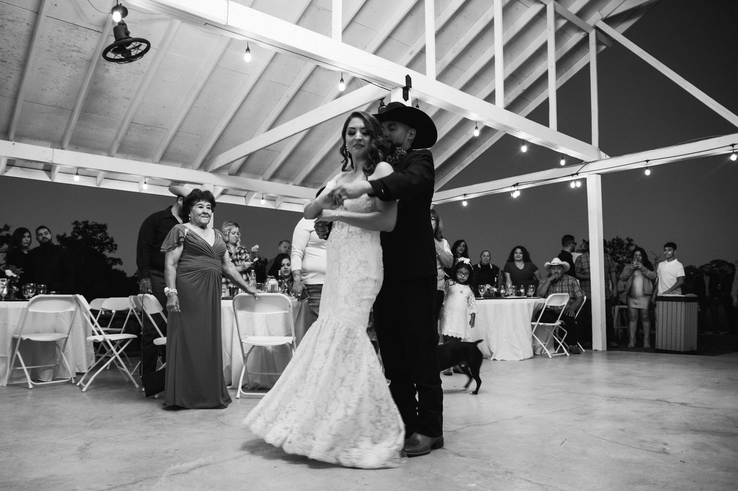 Black and white photo of newlyweds dancing in reception hall with guests seated at tables.