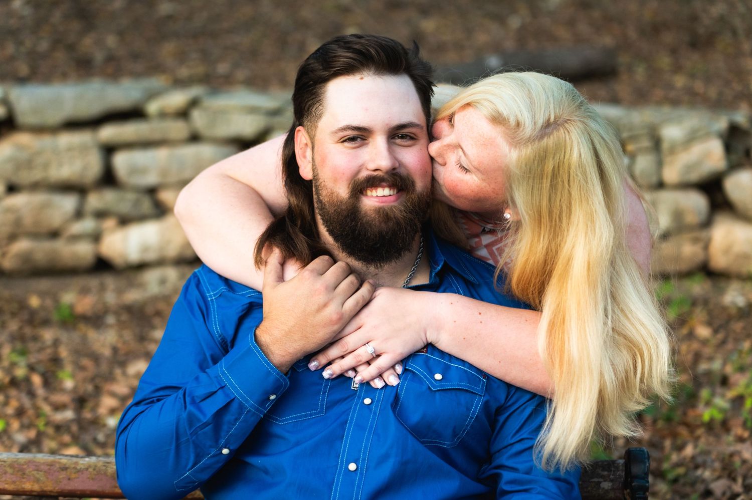 A romantic couple in matching blue outfits share an affectionate moment against a stone wall.