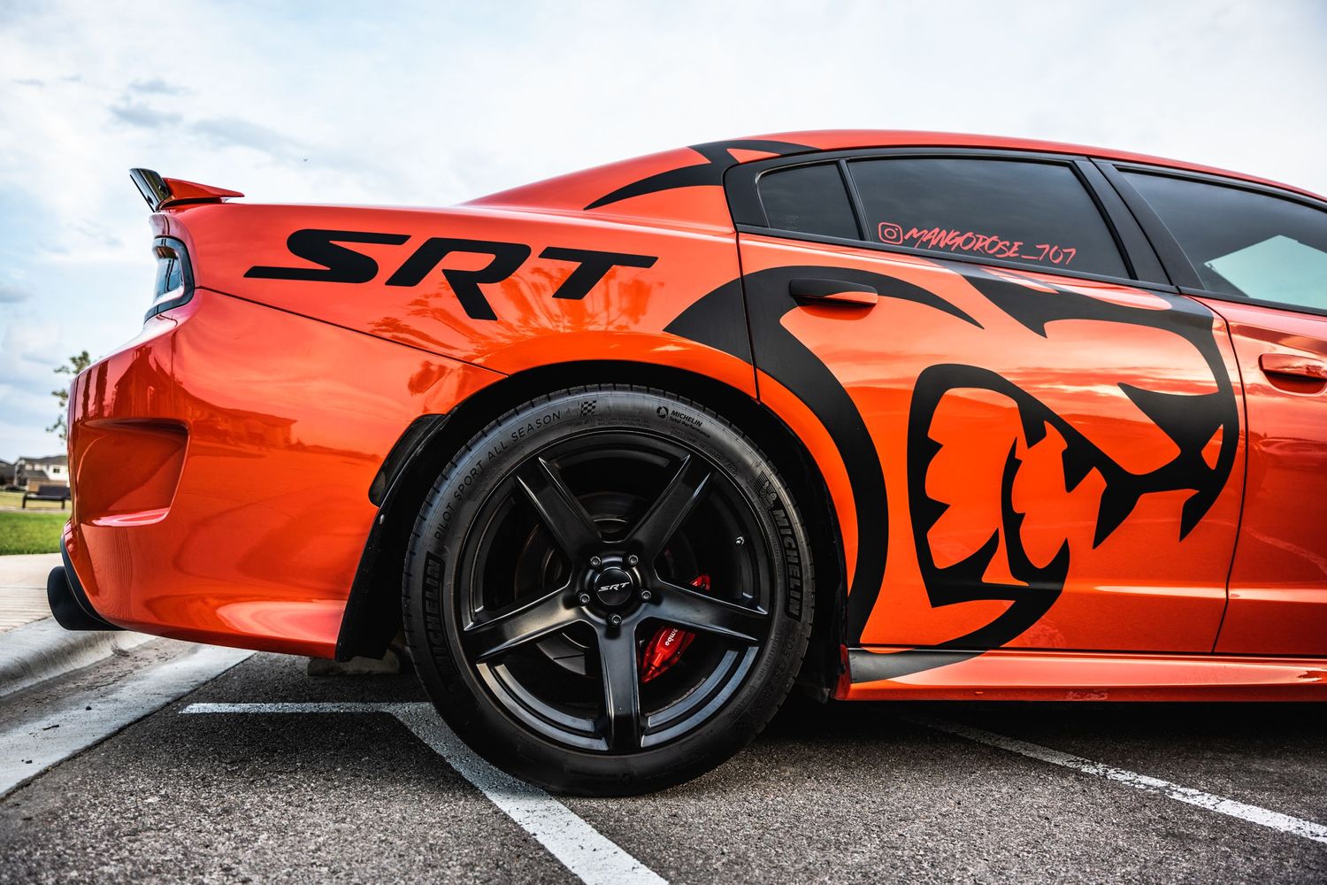 Side profile of an orange Dodge Charger SRT with black racing stripes and custom wheel design.