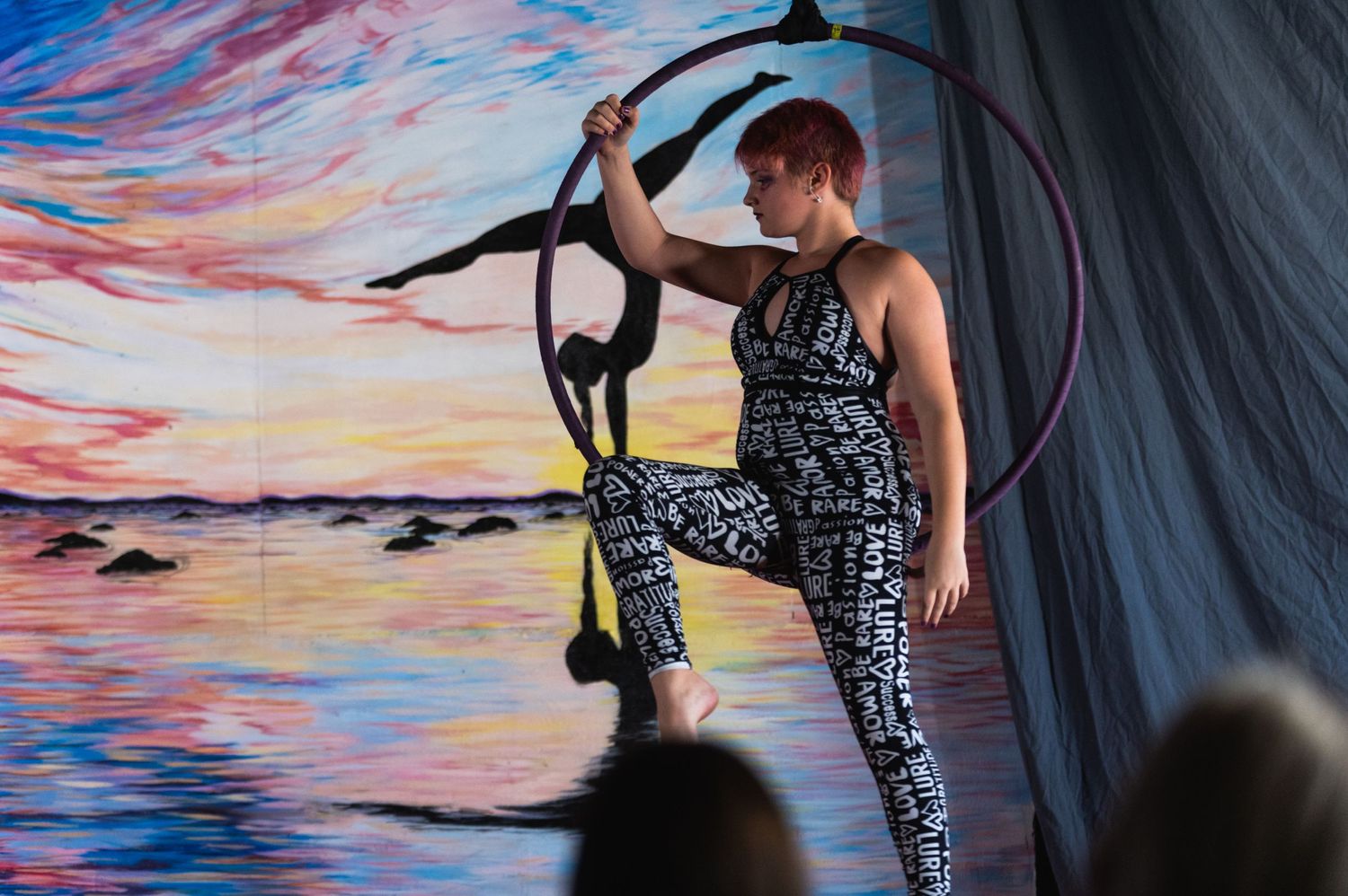 Performer in geometric print outfit demonstrates strength on aerial equipment during show.
