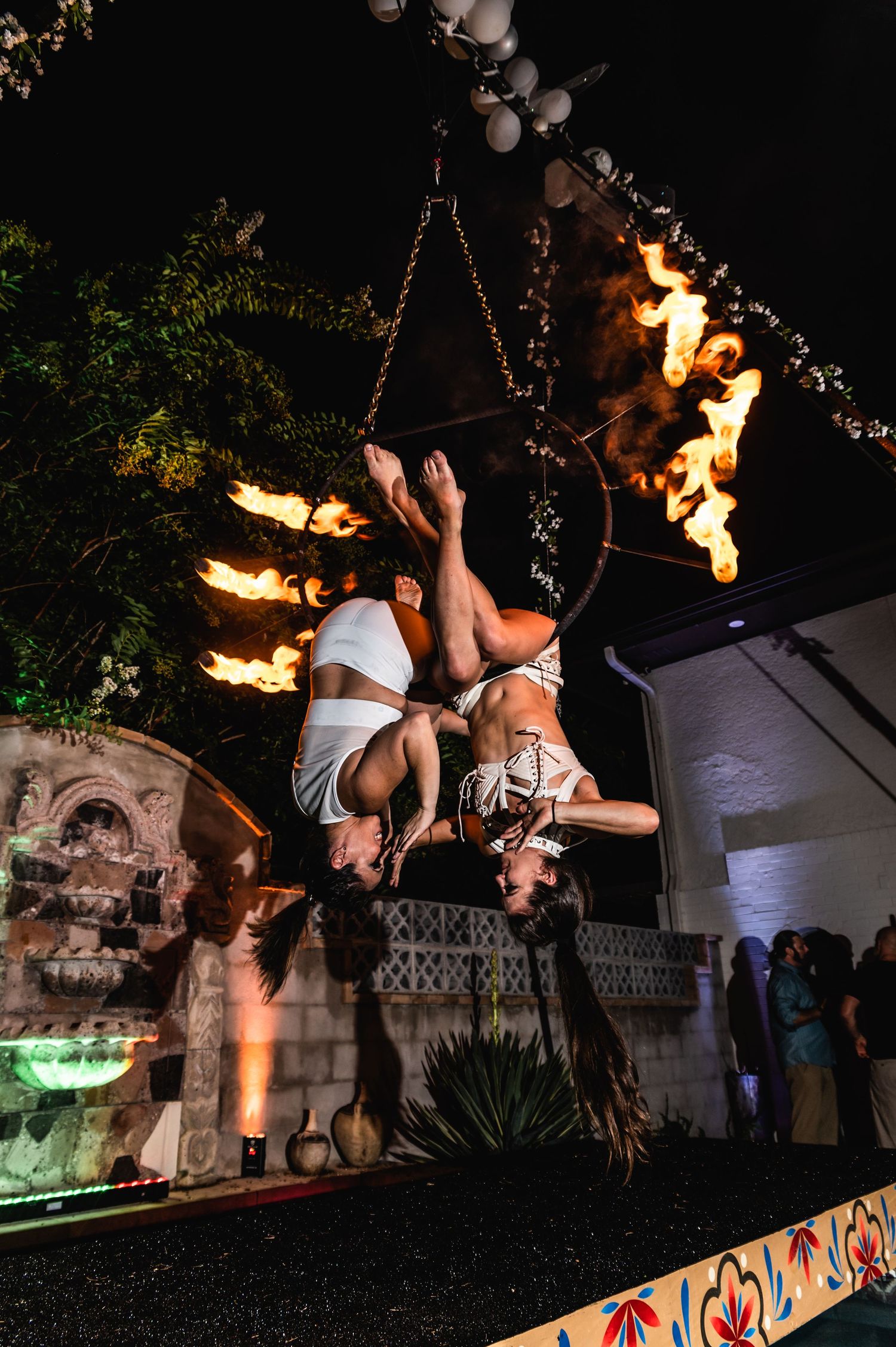 Two aerial artists perform synchronized moves with fire elements in outdoor venue.