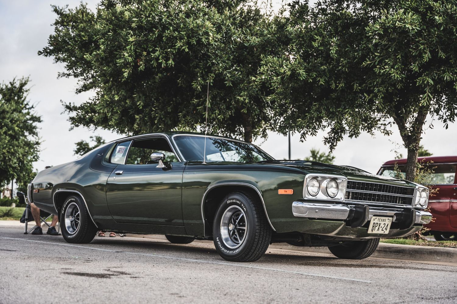 Classic Plymouth Road Runner muscle car in dark green with chrome wheels parked under trees.