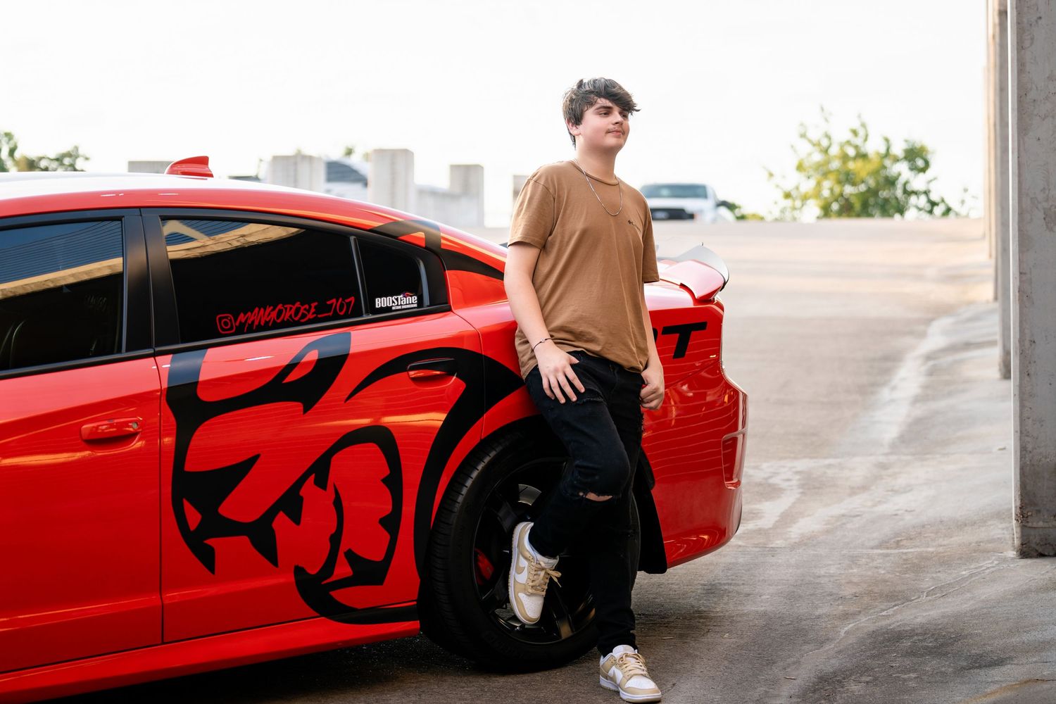 A casual portrait next to a modified red Dodge Charger with black graphics in a parking structure.