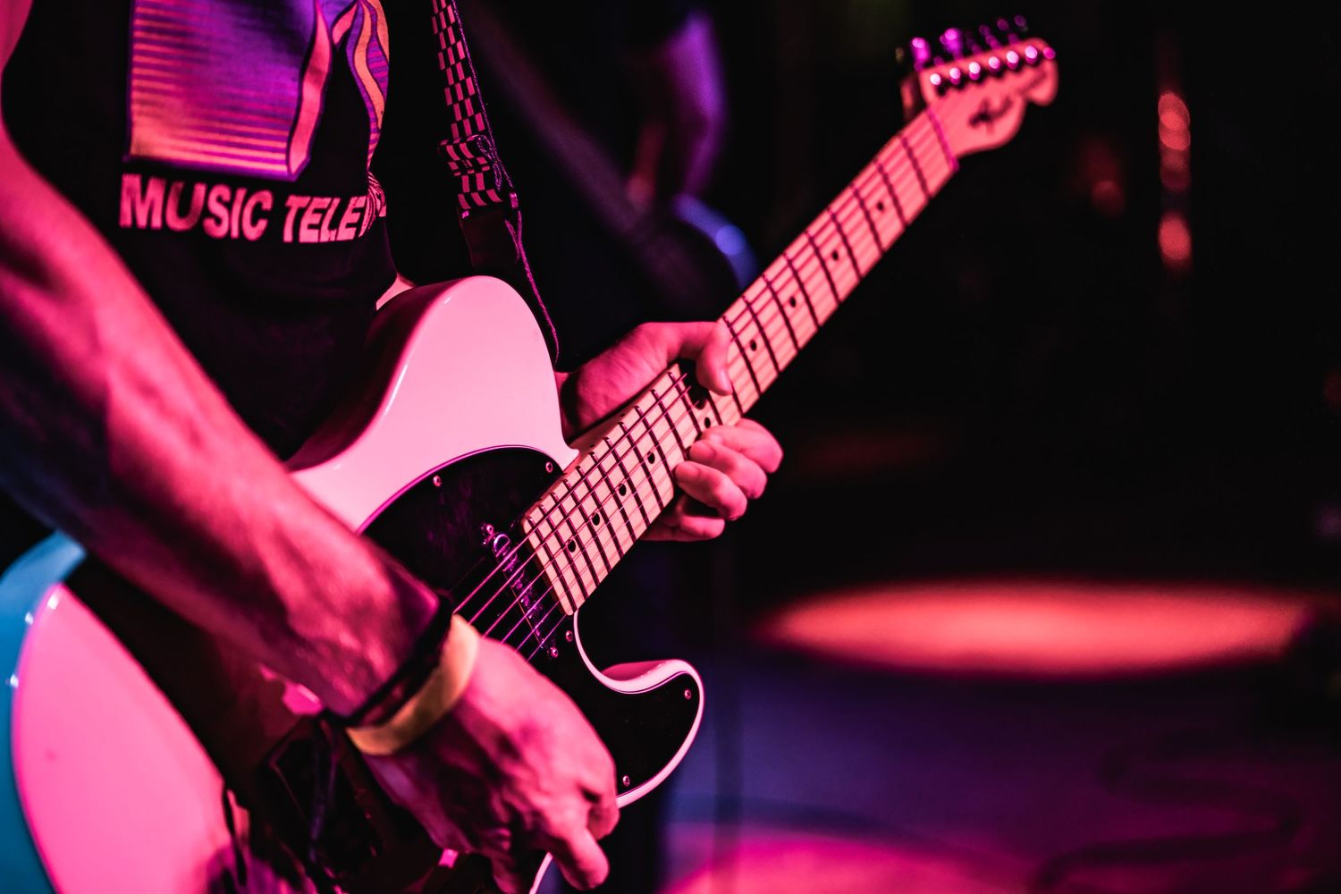 Close-up of an electric guitar being played under dramatic pink stage lighting.