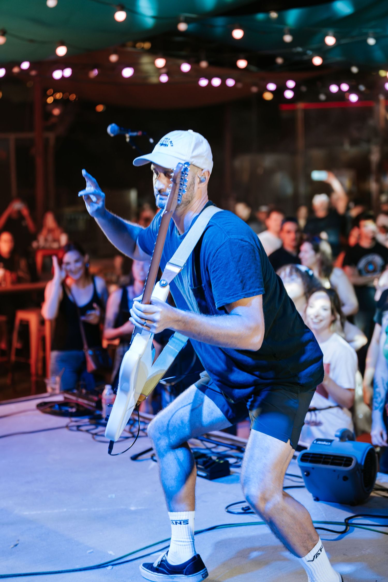 Musician in blue shirt and hat playing guitar on stage during live performance.