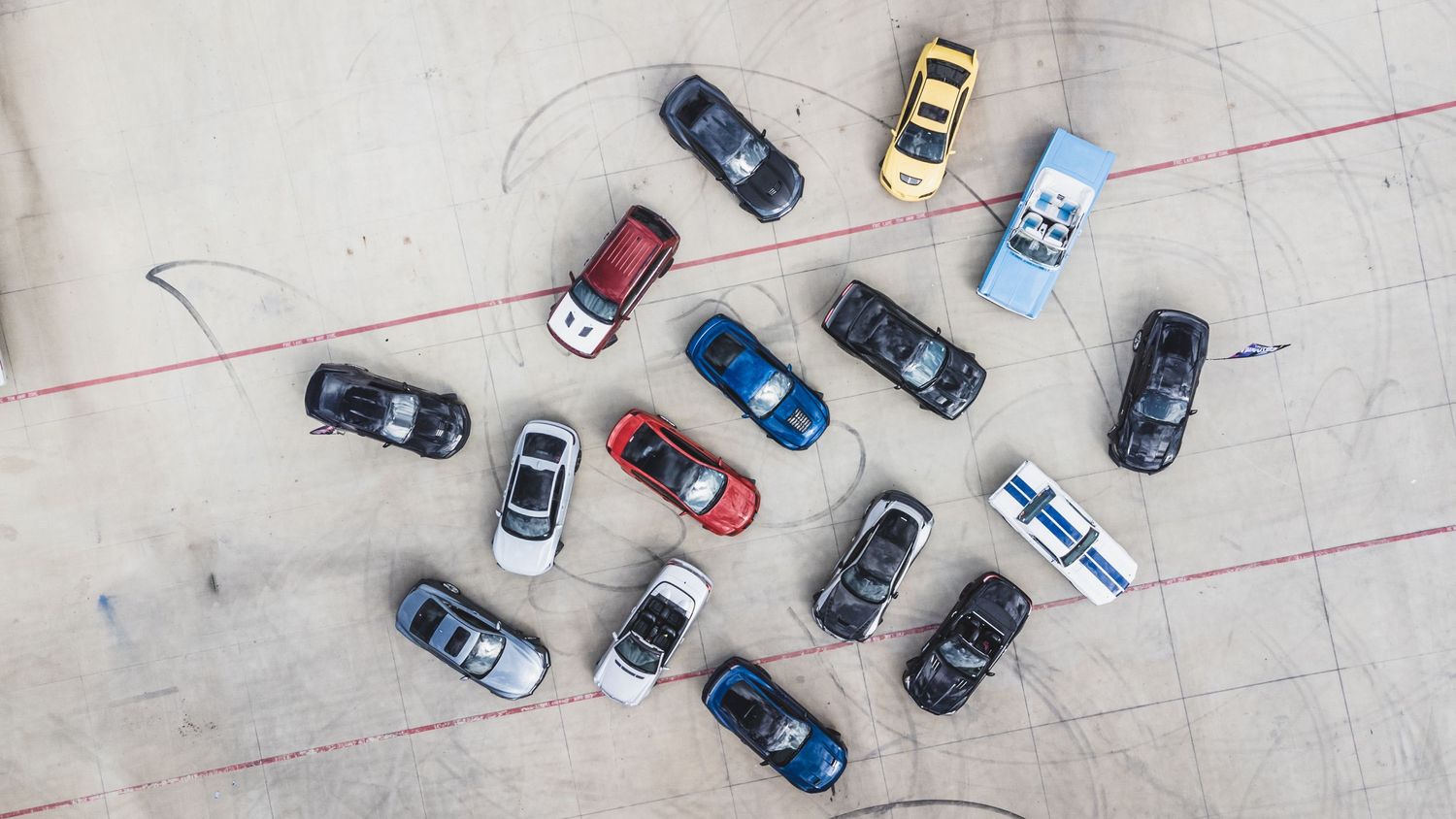 Aerial view of various colored cars arranged in casual formation on concrete surface.