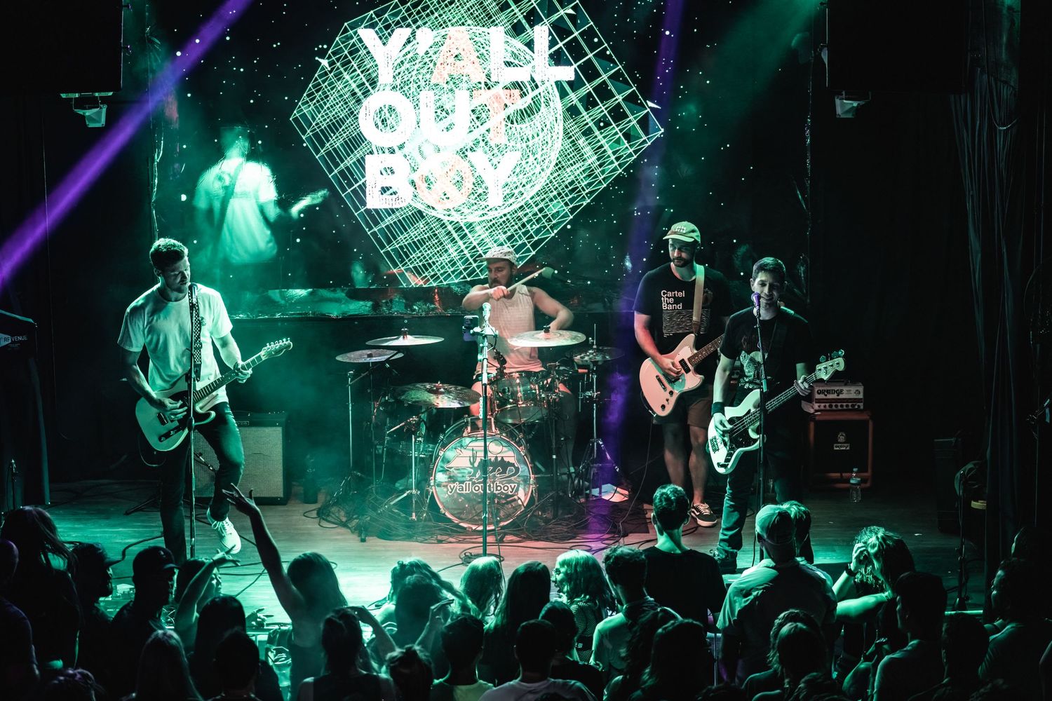 Rock band performs on stage with neon lighting and enthusiastic crowd at intimate venue.
