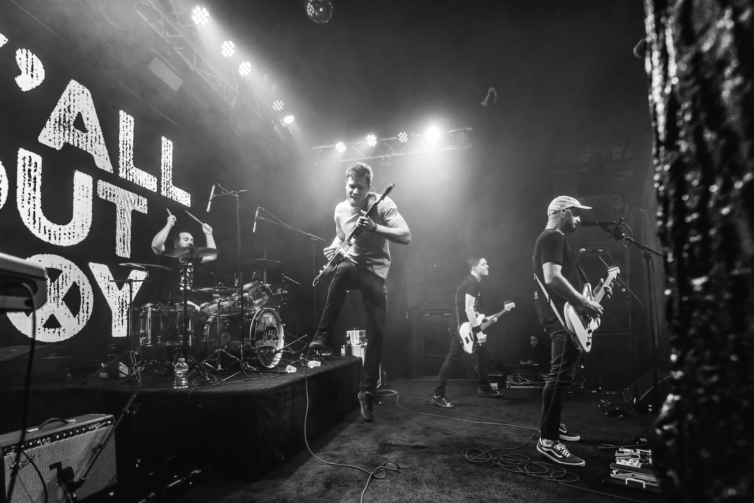 Black and white concert photo showing a band performing energetically on stage with dramatic lighting.