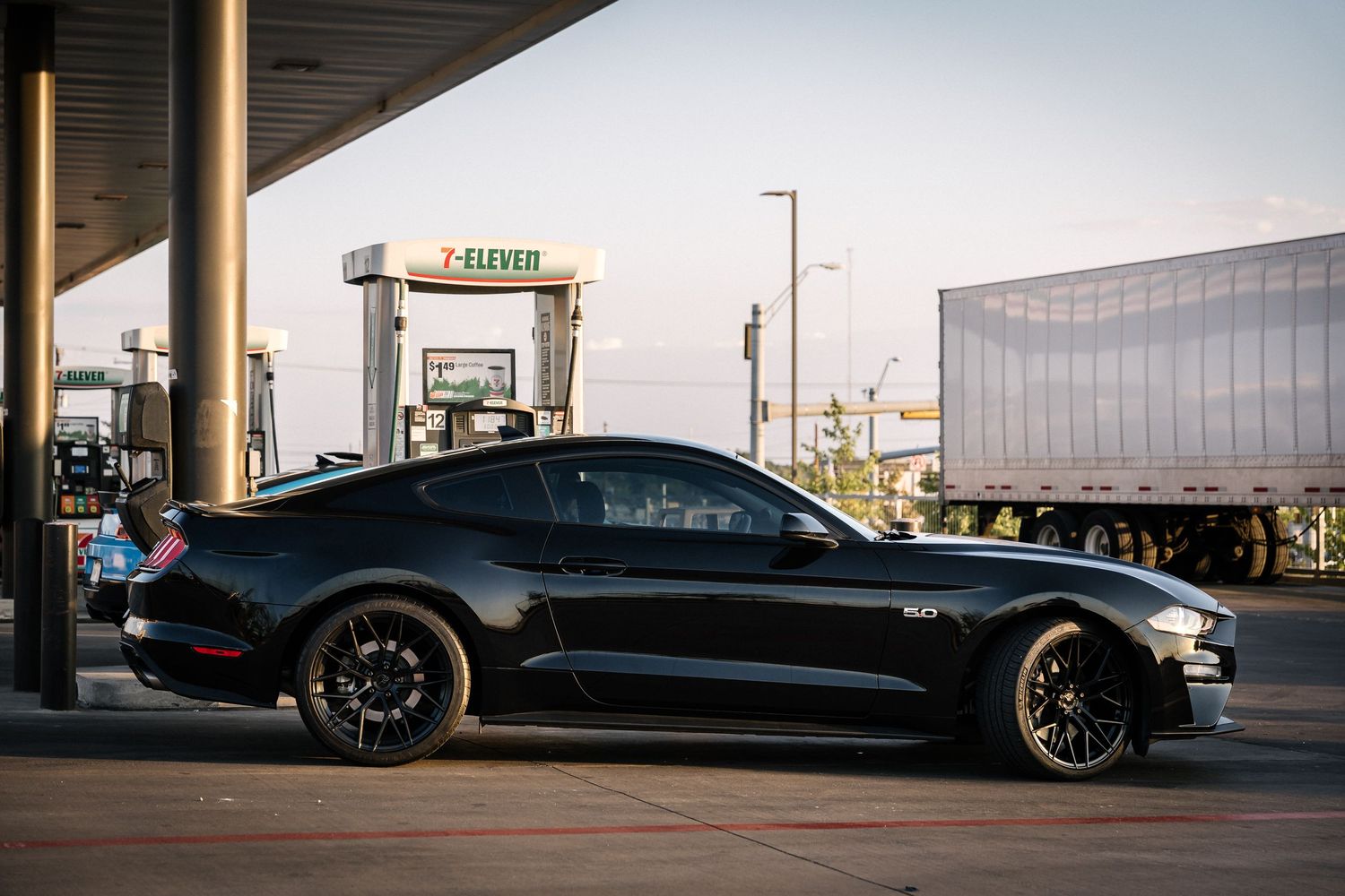 Black Ford Mustang parked at gas station during sunset.