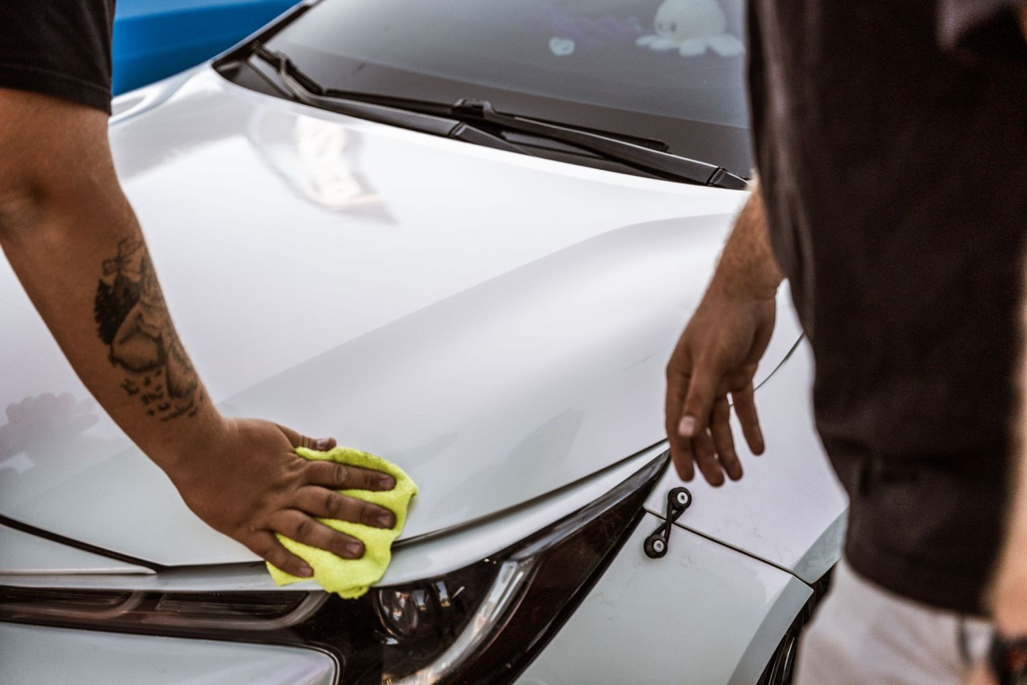 Close-up of hands detailing a car's headlight with a yellow microfiber cloth.