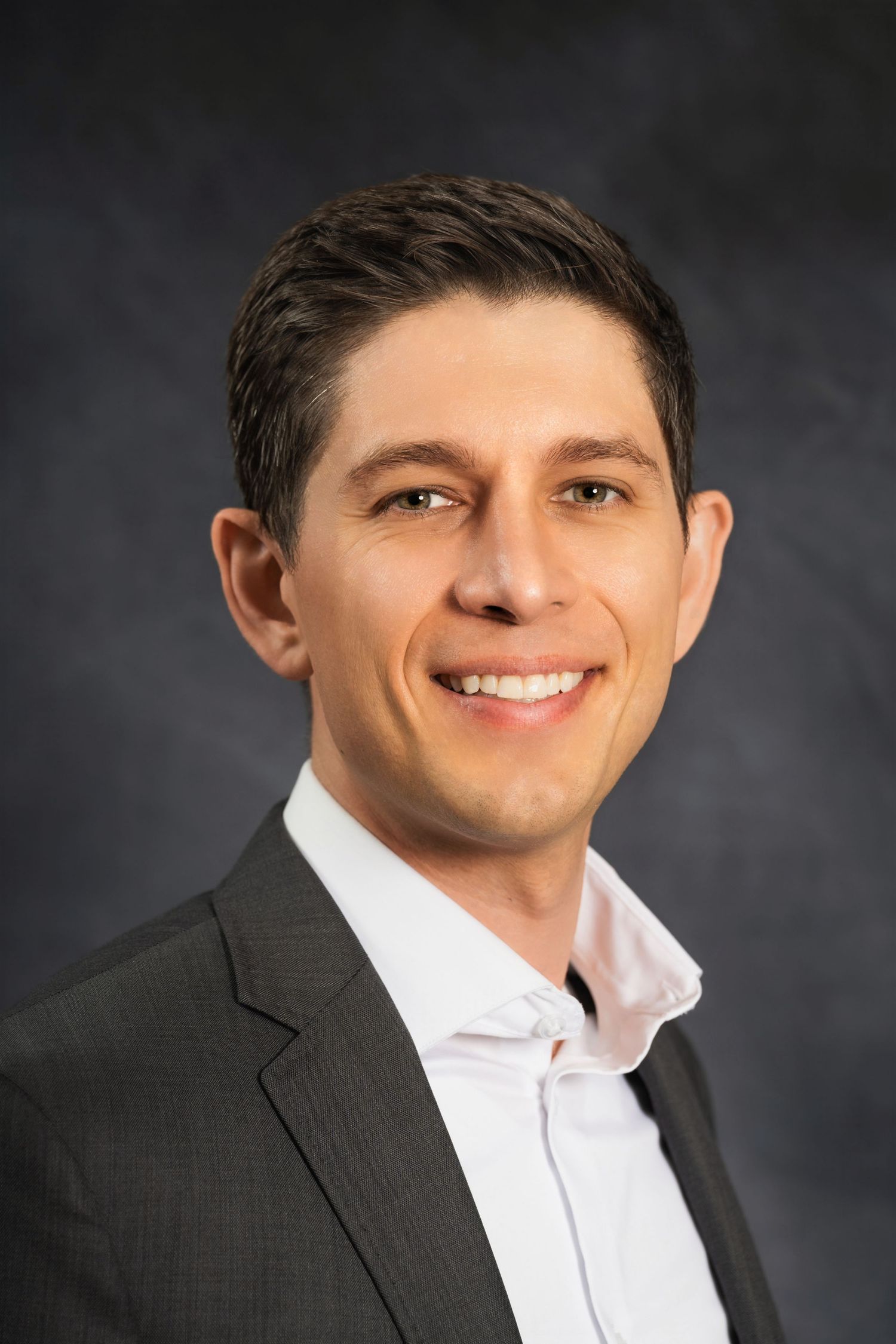 Professional headshot featuring business casual attire against a dark studio background.
