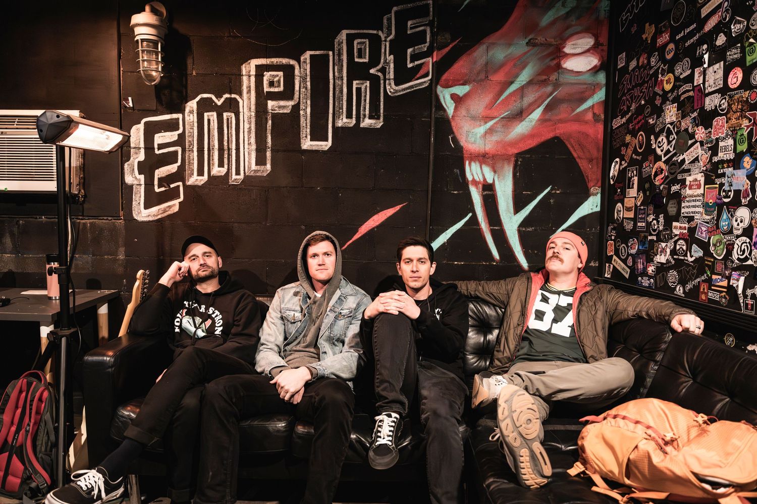 Band members sitting casually on a couch against a wall decorated with Empire branding.