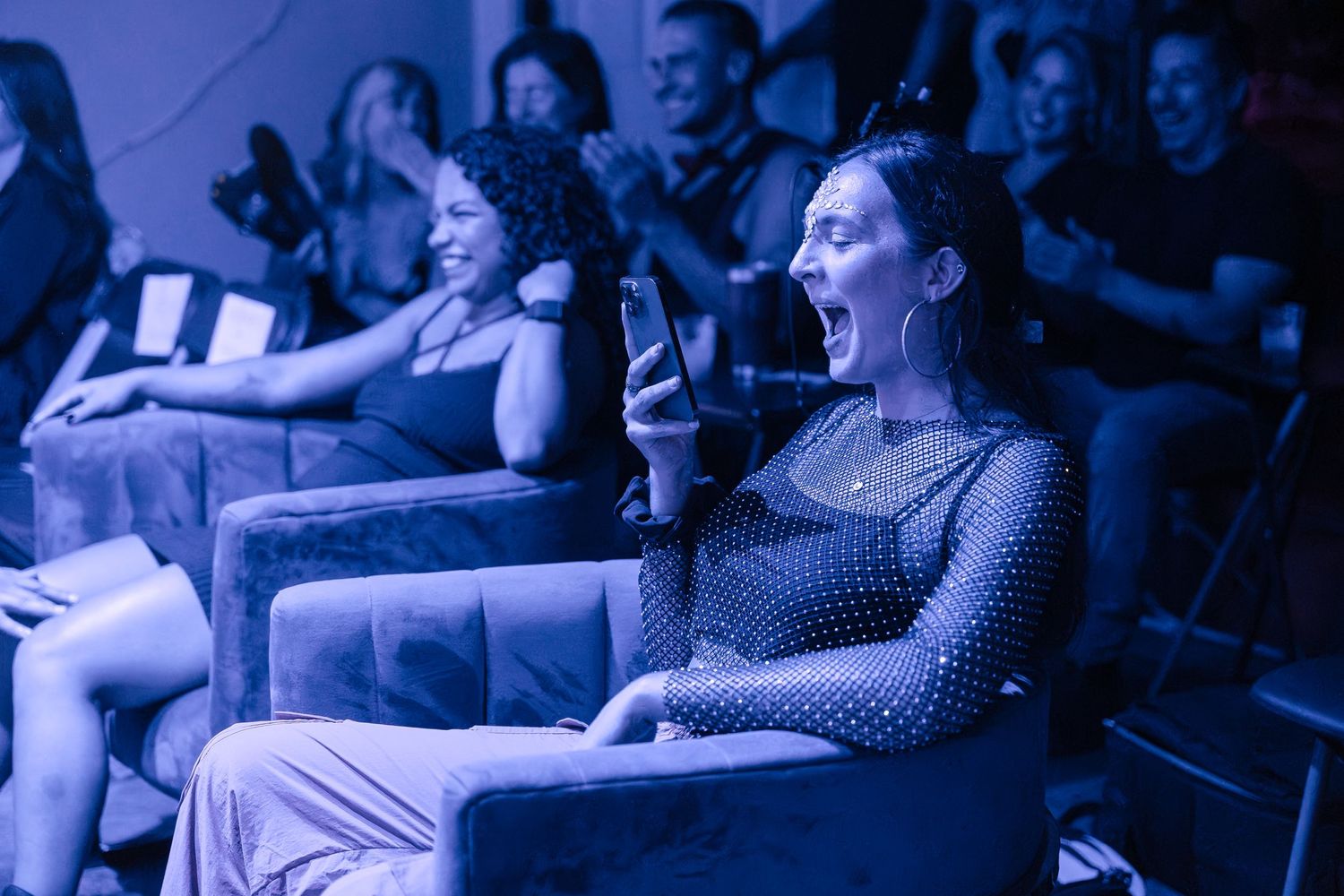 Audience member holds phone while watching performance in blue-tinted theater.