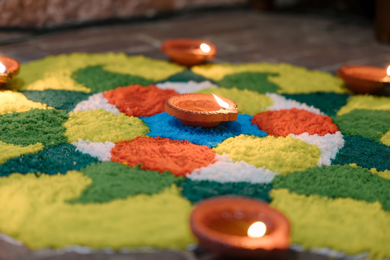 Colorful rangoli design with lit diyas displaying vibrant yellow, green, and orange powders.