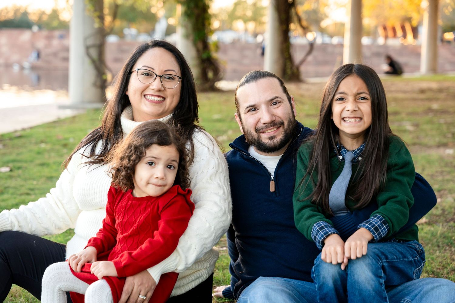 Family sitting together outdoors on a sunny autumn day wearing casual clothing.
