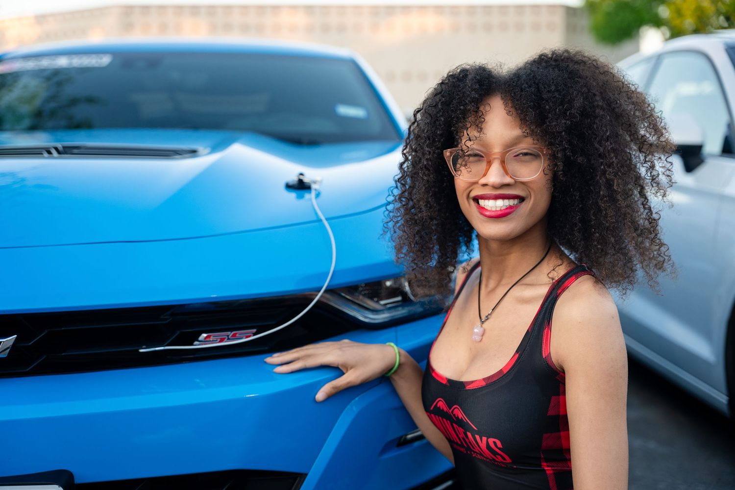 Person posing beside bright blue sports car in parking lot.