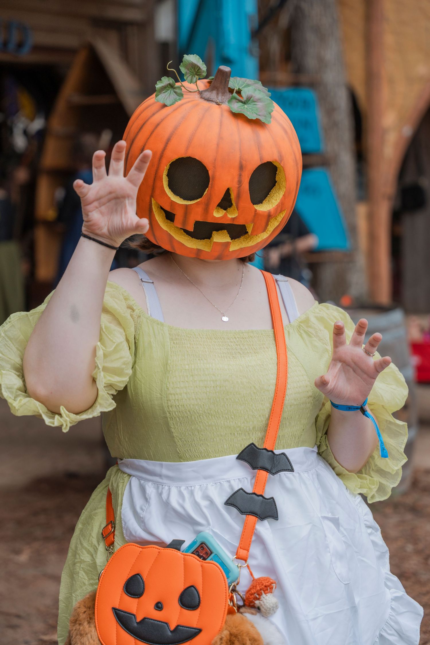Person in yellow dress wearing a jack-o'-lantern head costume with matching pumpkin purse.