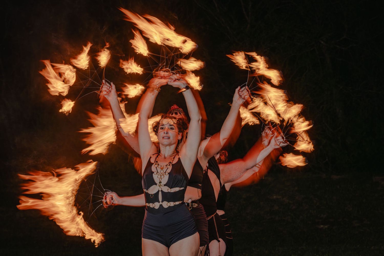 Fire dancer performing with flaming props at night, wearing skeleton costume, creating dramatic orange flame effects.
