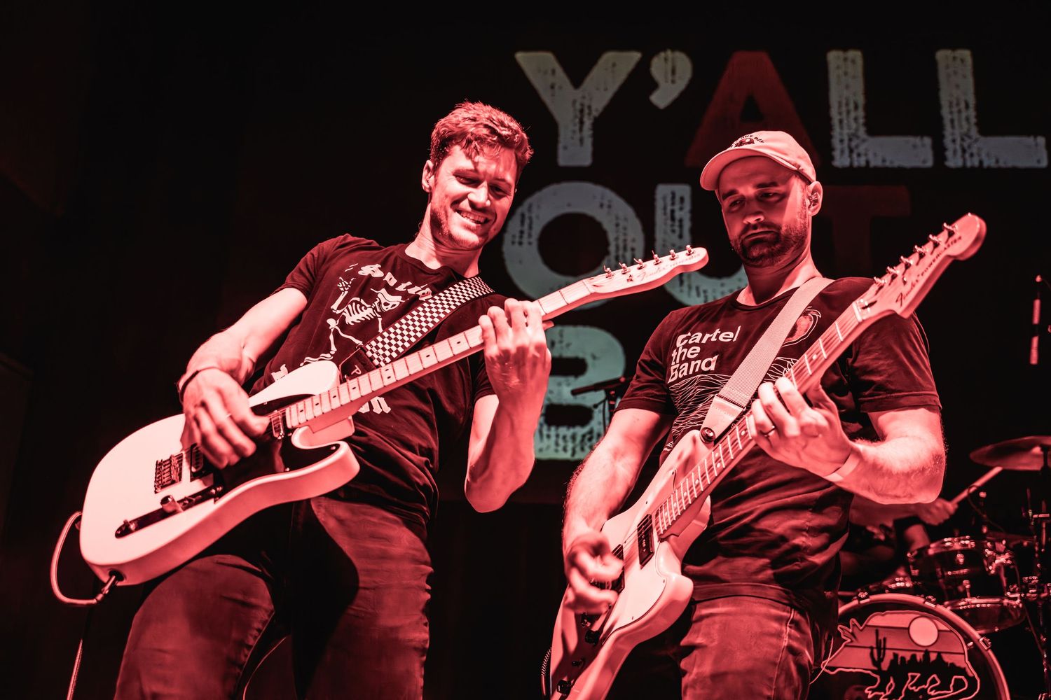 Two guitarists perform on stage in dramatic red lighting during a live music performance.