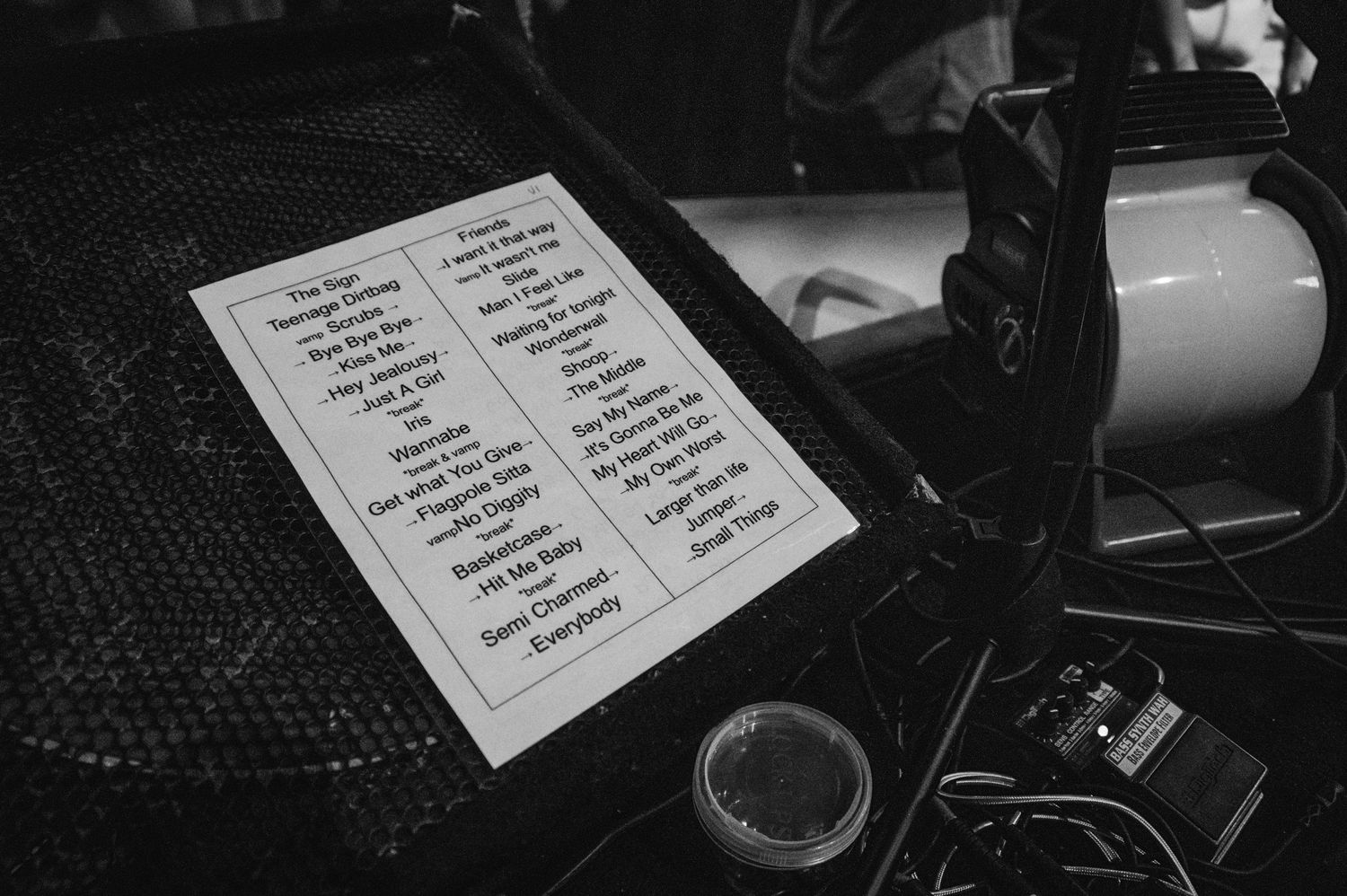 Black and white photo of a setlist on stage with a glass and equipment visible.