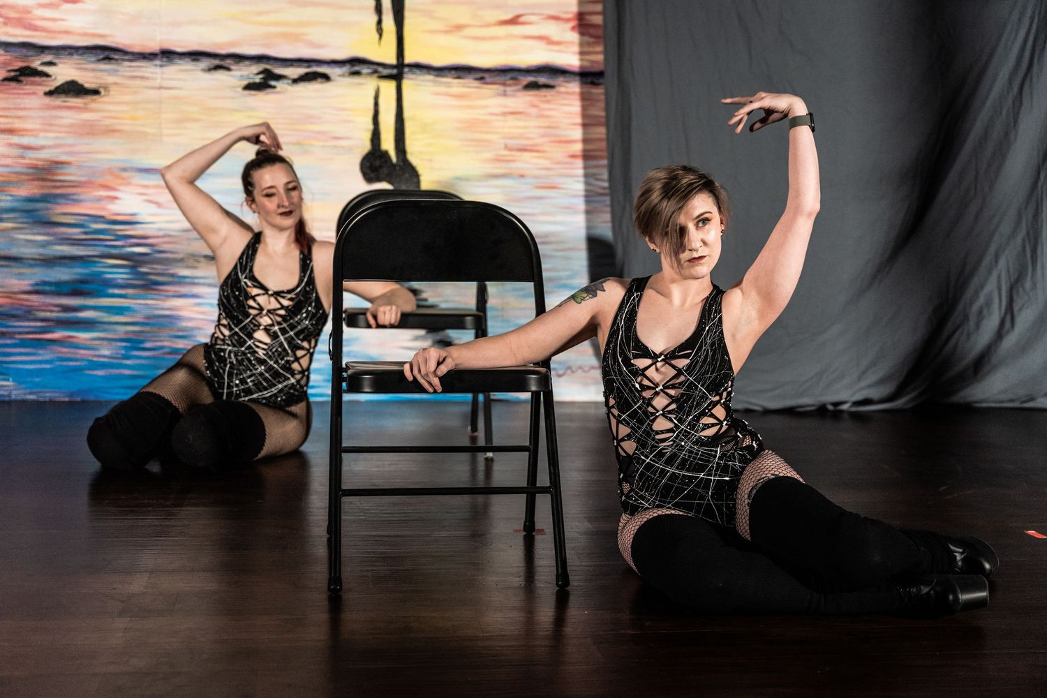 Two dancers in black lace costumes perform a synchronized floor routine against a sunset backdrop.