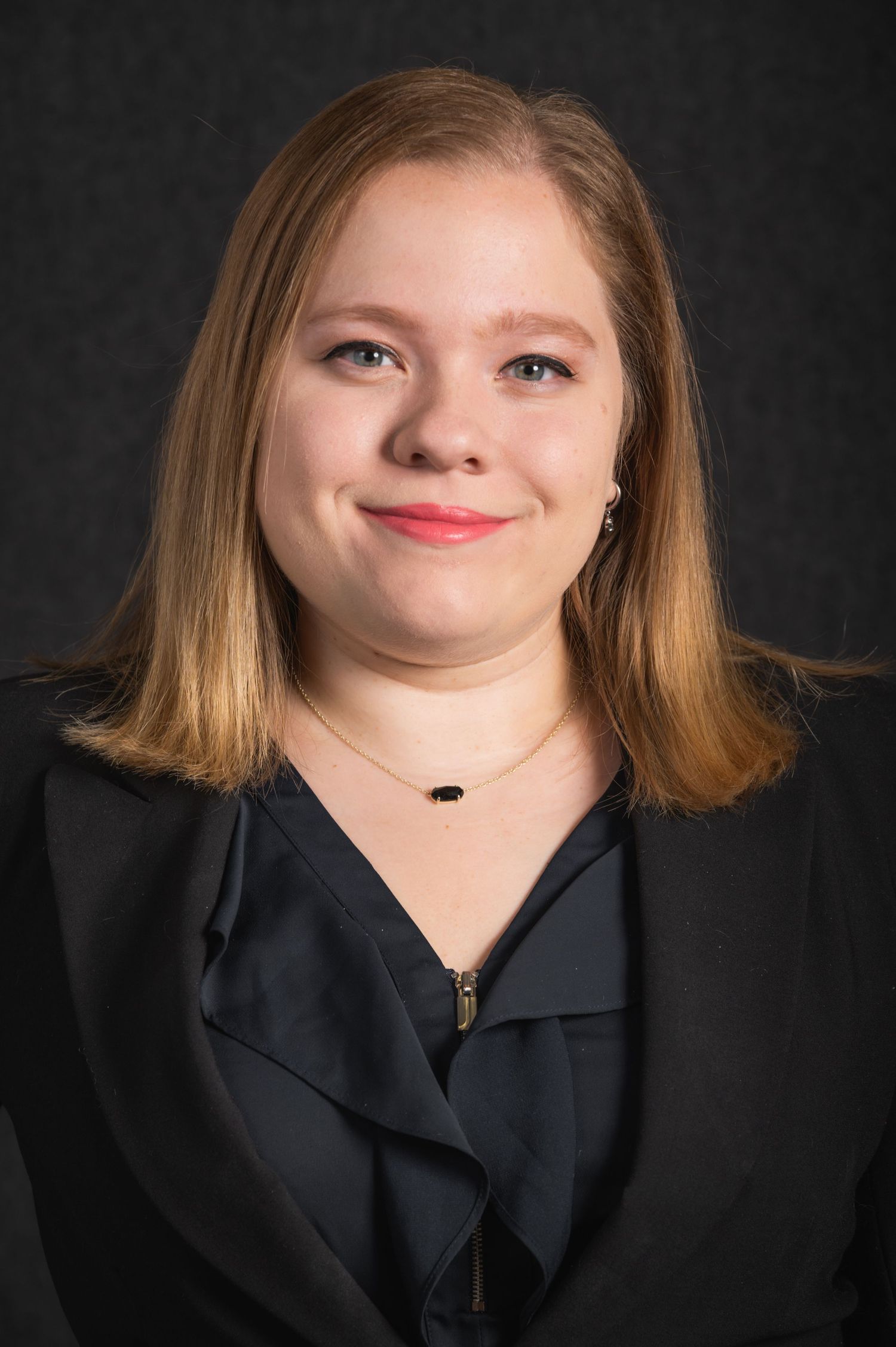 Professional headshot of someone wearing a black blouse against a dark background.