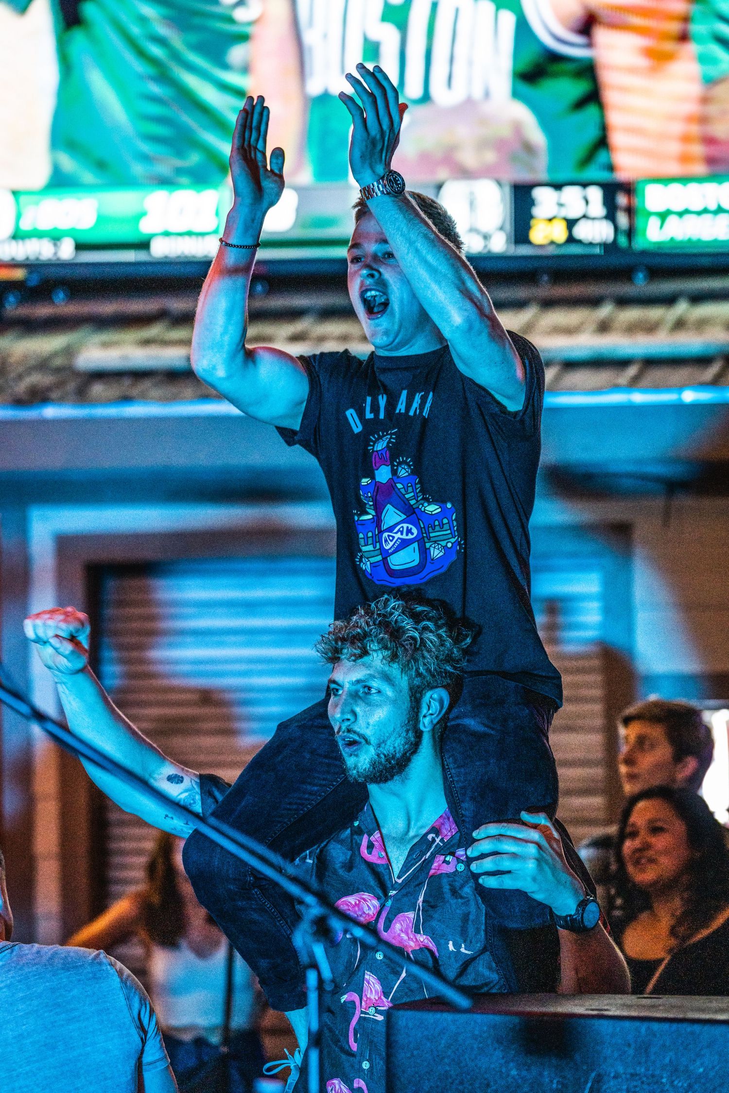 Concert crowd member raises hands in blue lighting during energetic performance.